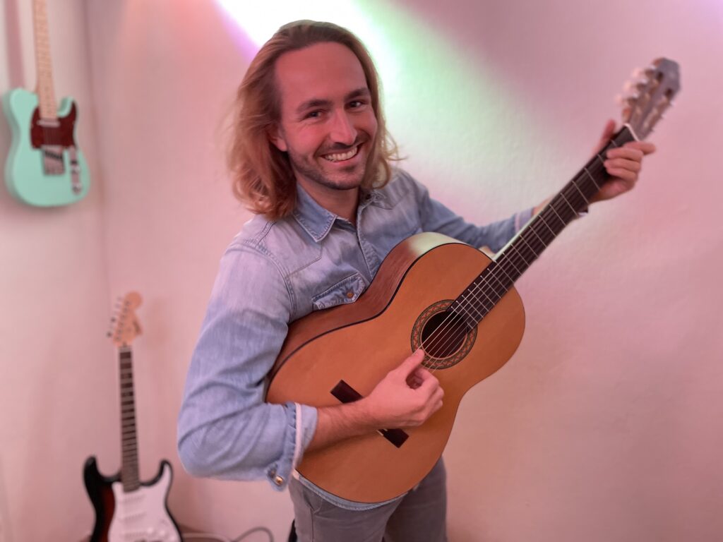 Akustik und E-Gitarren im Hintergrund und im Vordergrund ein Gitarrenlehrer in Bergisch Gladbach in der RhythmusFabrik.