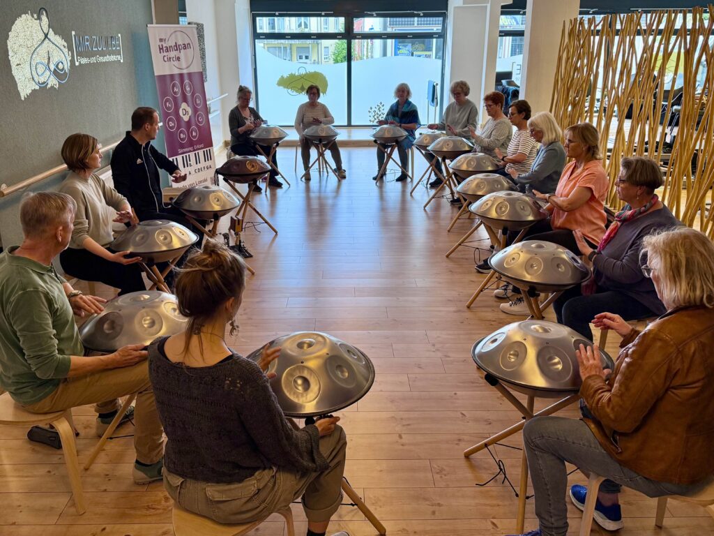 Ein Handpan Lehrer in Bergisch Gladbach unterrichtet eine Gruppe mit Handpan der Marke Sela. Seitlich im Hintergrund sieht man die Werbung myHandpanCircle.