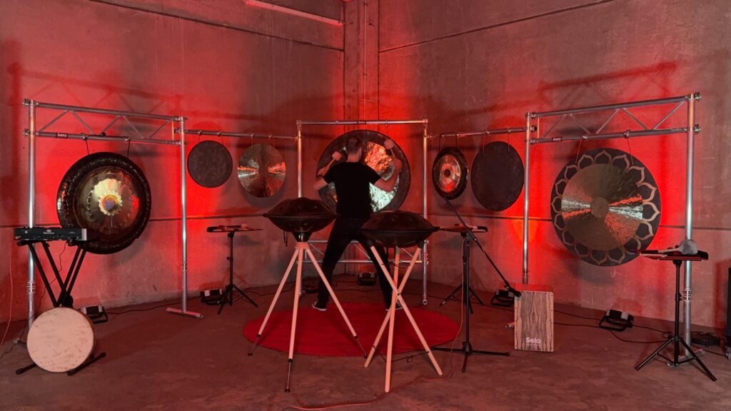 Ein Mann spielt bei einem Event verschiedene Gongs. Er benutzt Feng Gongs, Tamtam Gongs und Symphonie Gongs.